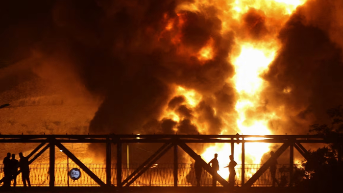 Люди наблюдают с моста за тем, как после израильских ударов по Ирану на нефтебазе «Шаран» поднимается пламя, Тегеран, Иран, 15 июня 2025 года