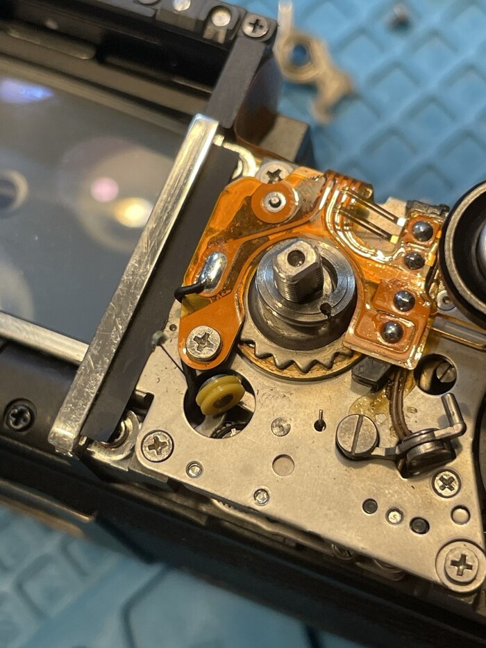 тут видна система блоков и торчащая проволочка. Крутилка выдержки крутит блок, вытягивая тонюсенький тросик, толщиной с волос, который идет в левую часть фотоаппарата.